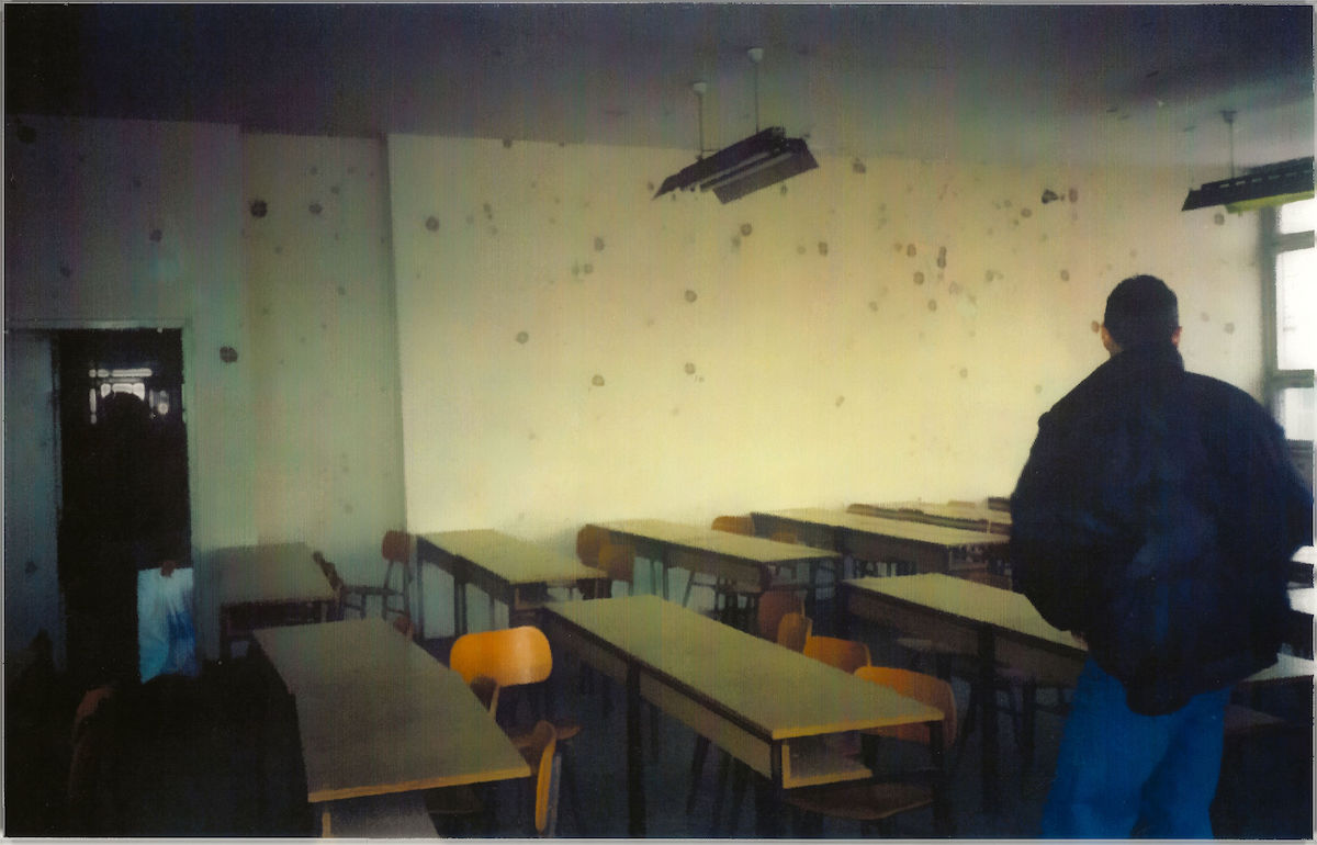 photo of an abandoned classroom with dozens of bullet holes in the wall